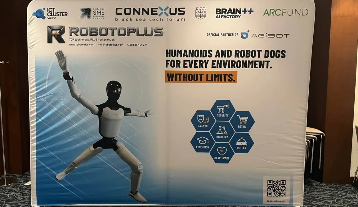 The Robotoplus stand wall at CONNEXUS 2026 in Varna: a white humanoid robot in a wide stance beside the line Humanoids and robot dogs for every environment, with the organisers' logos along the top.