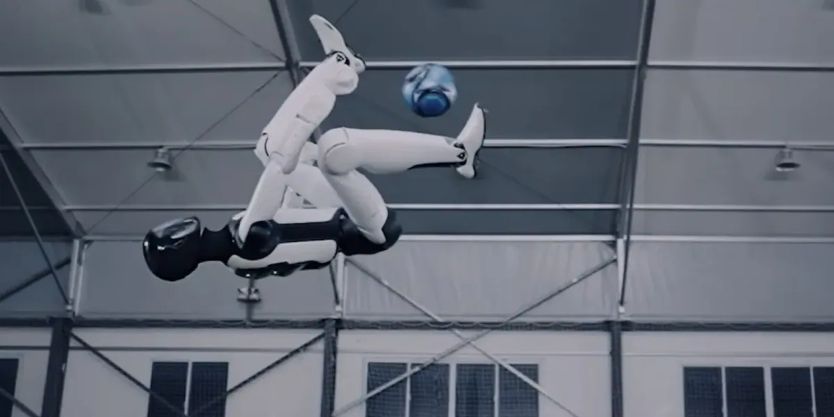 The AGIBOT A3 humanoid inverted in mid-air inside a netted training hall, one leg extended towards a ball